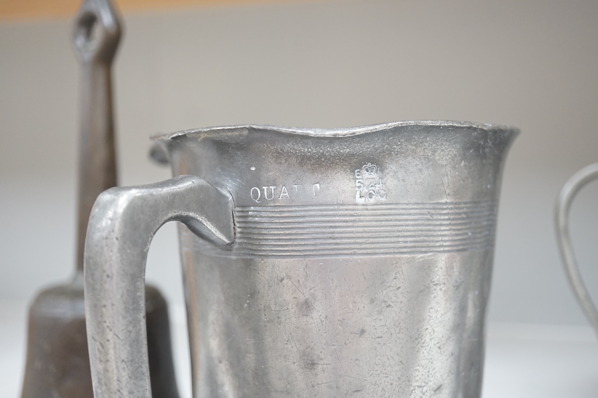 Six items of 18th century and later pewter including a jug, candlesticks, a pint measure, and a bronze hand bell, 24cm high. Condition - fair.